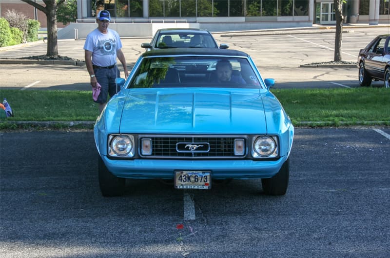 Someone sitting inside a light blue Mustang on display