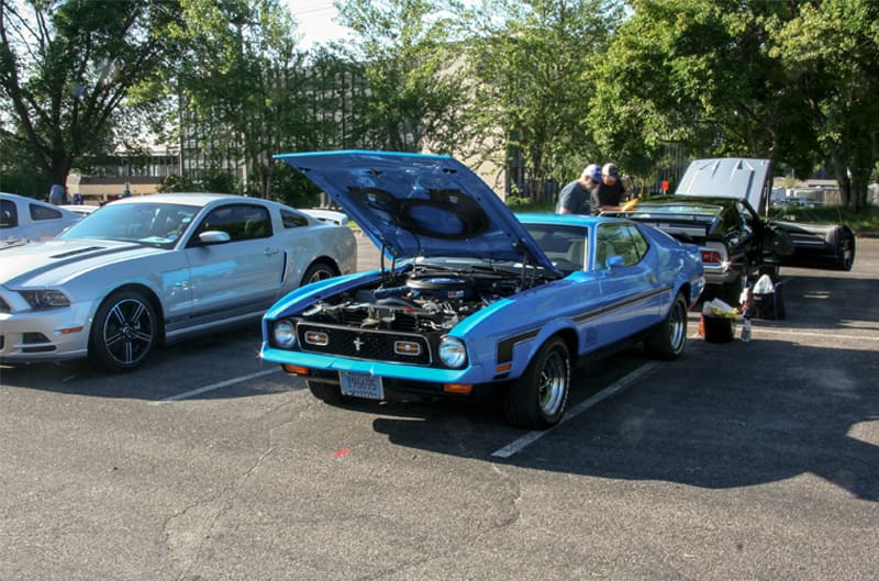 A front side view of a blue Mustang on display with the hood up