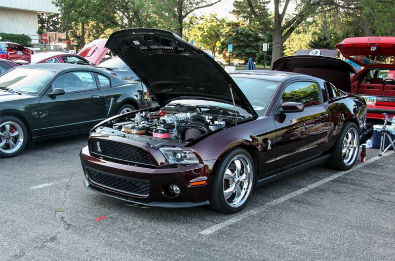 A front side view of a maroon Mustang on display with the hood and trunk open