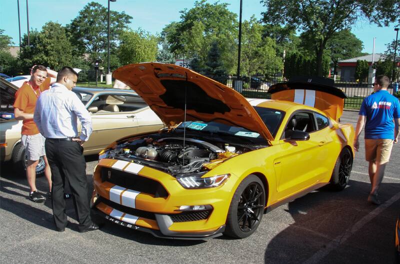 People admiring a yellow and white Mustang on display with the hood up