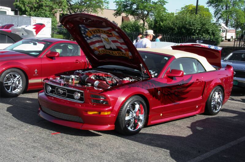 A red Mustang on display with a bald eagle illustration on the bottom of the hood