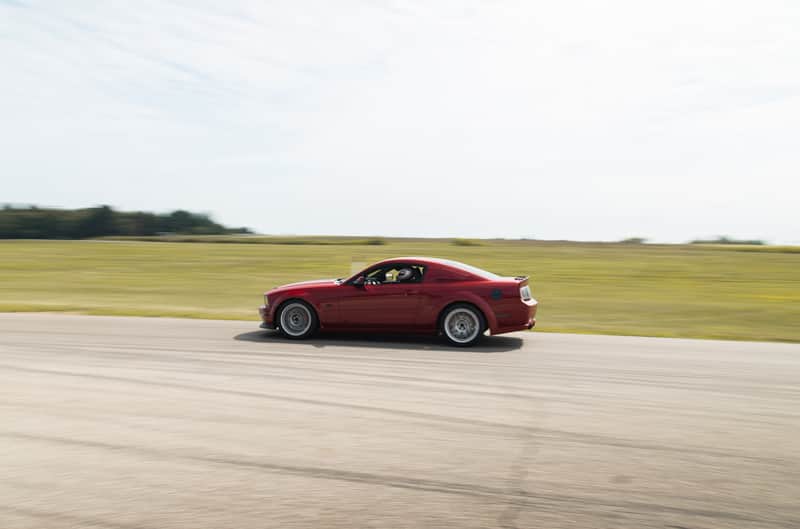 A side view of a red Mustang racing down the track