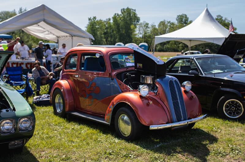 A front side view of a classic orange vehicle with blue flames on the side