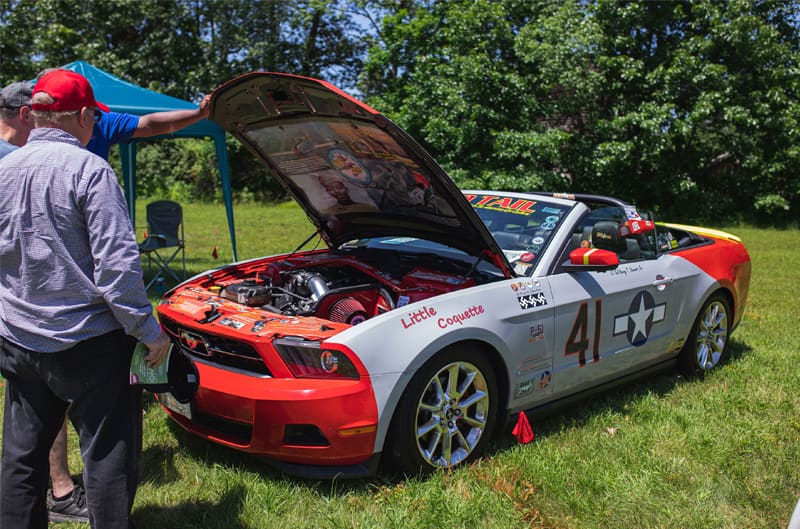 A silver and red Mustang on display with the hood up