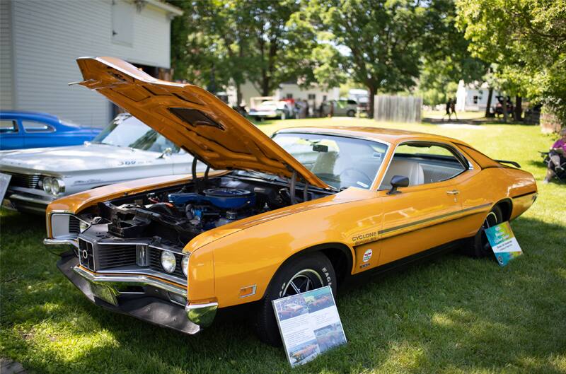 A front side view of a classic yellow Mustang on display with the hood up