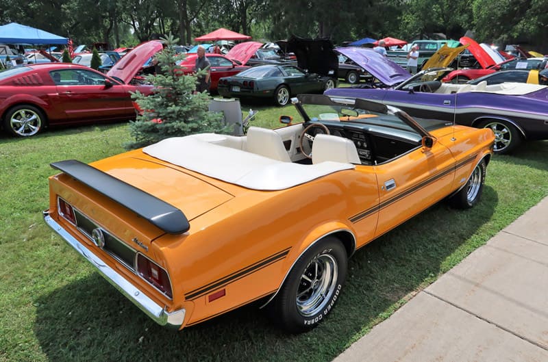 A rear side view of a classic orange convertible on display