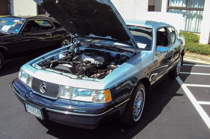 Front of a light blue Mercury with hood open in the parking lot