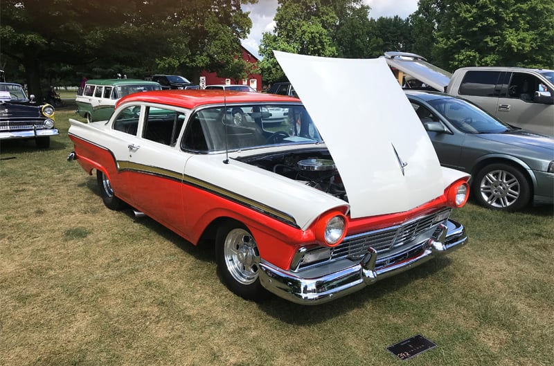 Front profile of a red and white Lincoln with hood open parked on grass