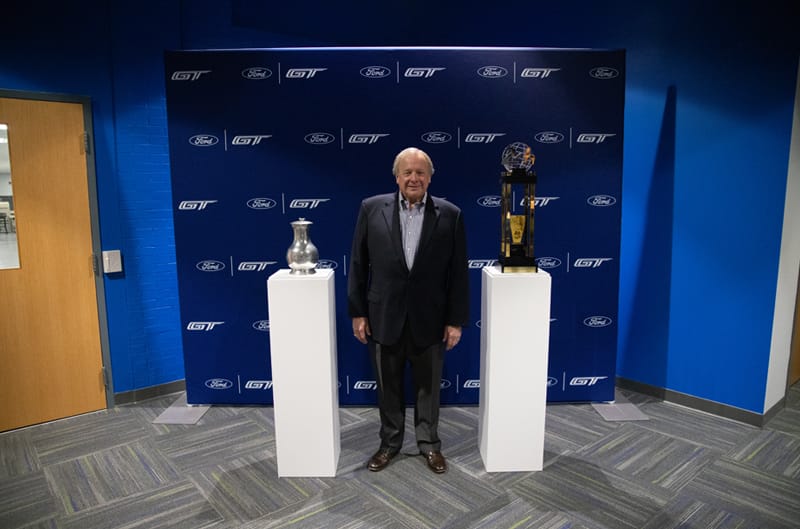 Edsel Ford II standing in front of a Ford GT back drop in between two trophies