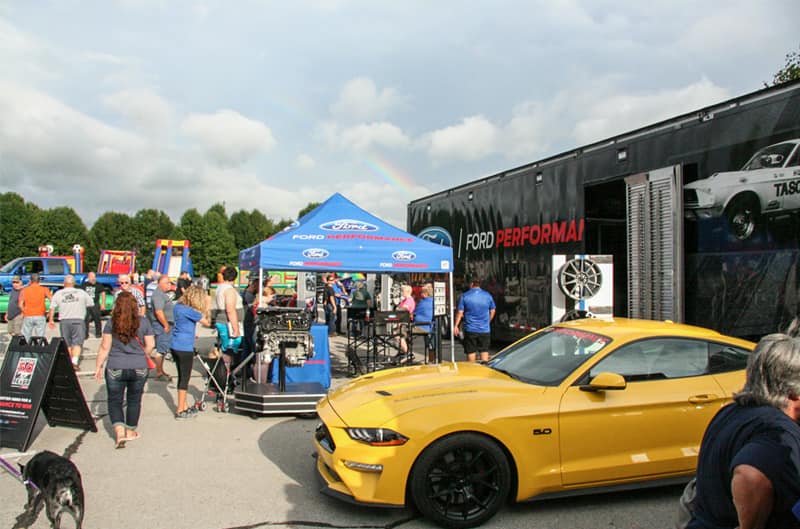A side view of a yellow Mustang on display next to a Ford Performance booth