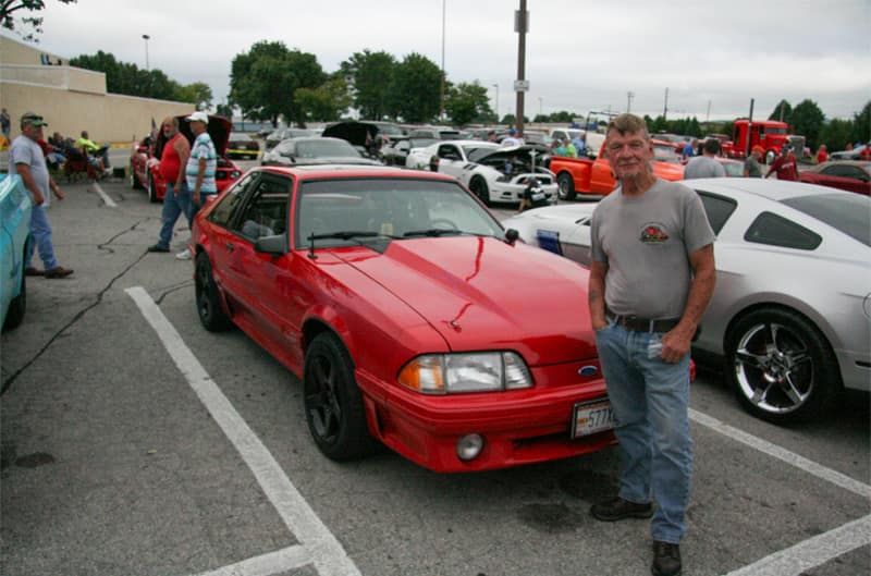 A man taking a photo with a classic red Mustang