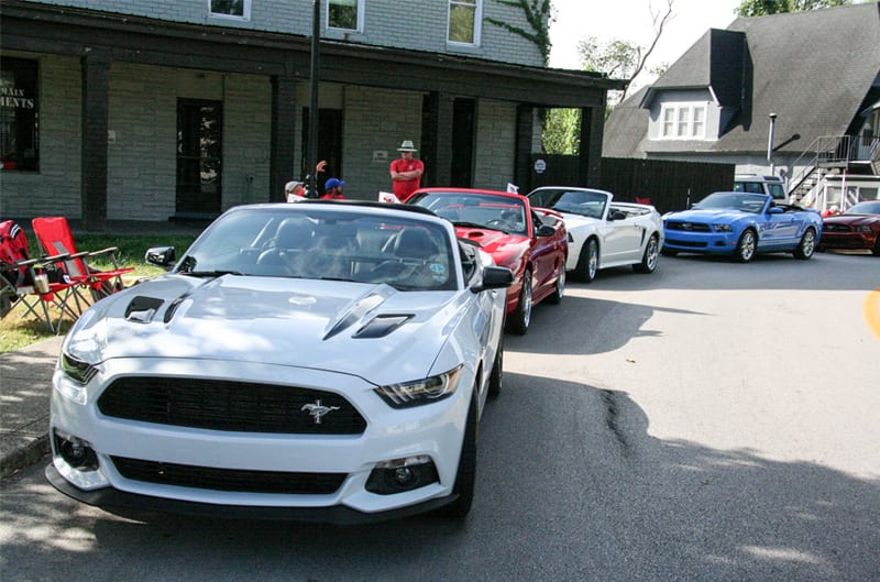A lineup of Mustangs driving down the road