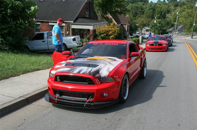 A red Mustang with an eagle illustration on the hood driving down the road