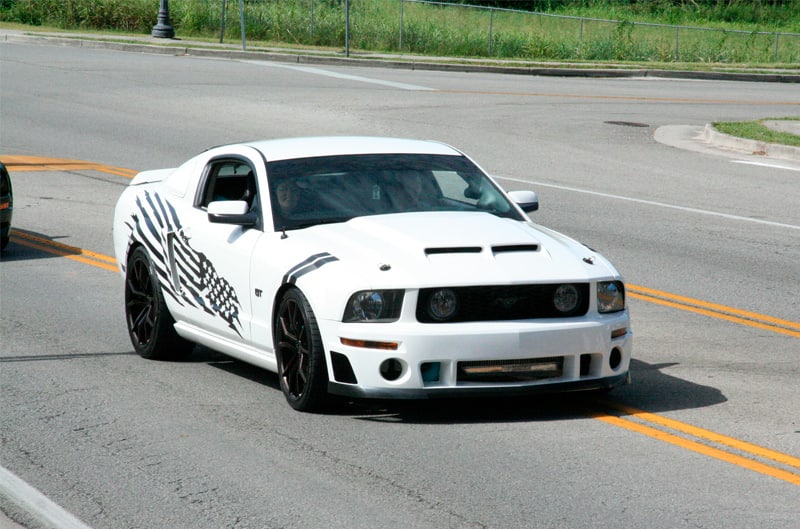 A white Mustang driving down the street