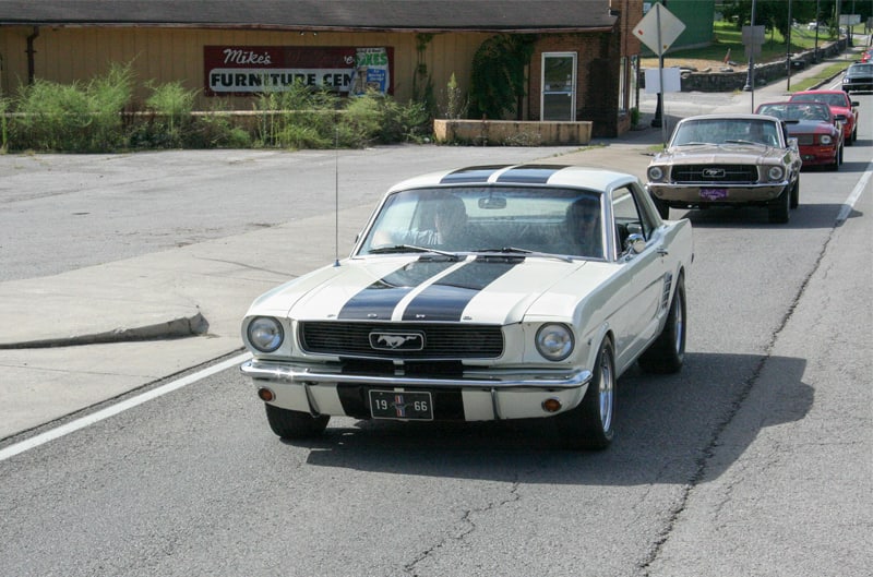 A white and black Mustang driving down the road