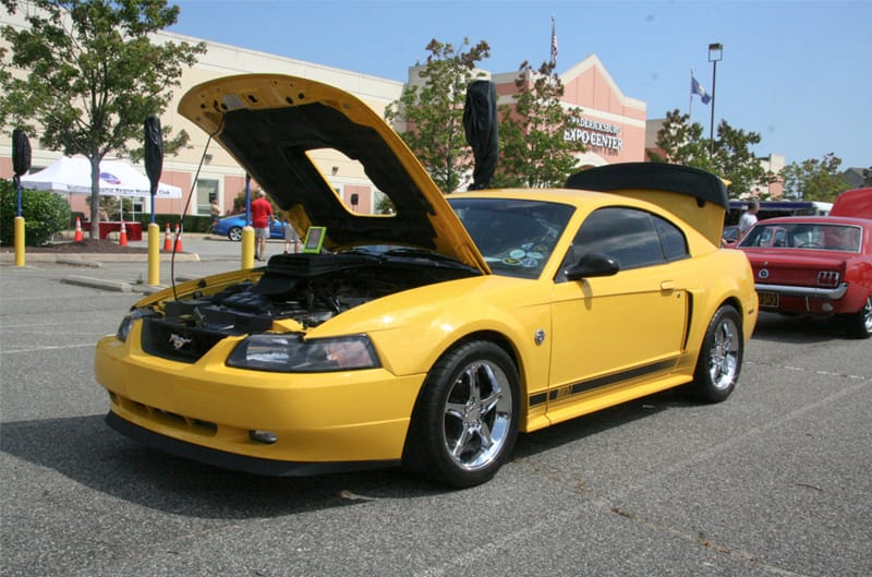 Front profile of yellow Mustang with hood open in parking lot