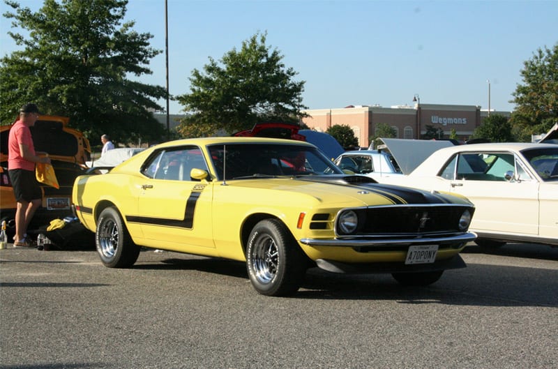 Front profile of a yellow Mustang with black stripe on hood in parking lot