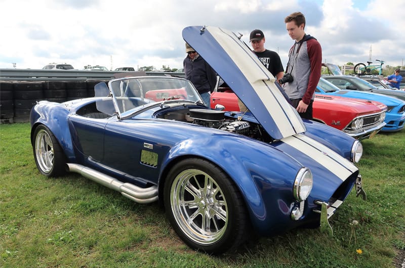 Front profile of a blue Shelby Cobra with white stripes parked on the grass