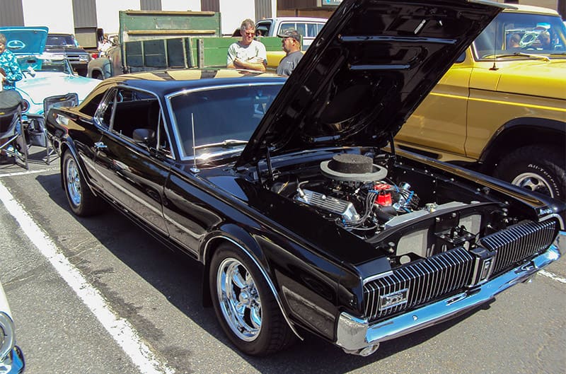 A classic black Mustang on display with the hood up