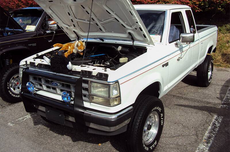 A white Ford truck on display with a stuffed animal under the hood