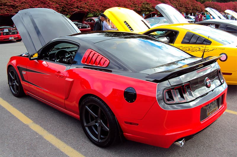 A rear side view of a red and black Mustang