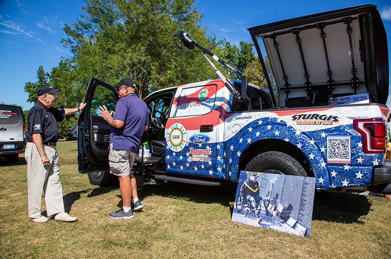 Two men standing in front of an American Flag painted F150 parked on the grass