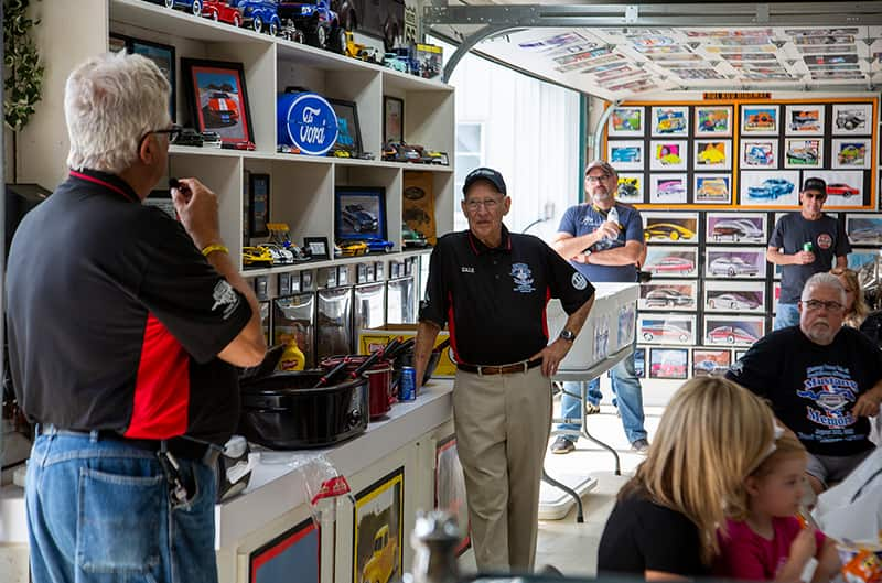 Men standing in front of shelves of diecast Fords in a garage of people