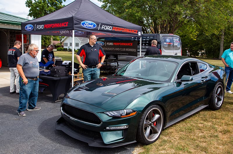 Front profile of a green Mustang Bullitt in front of Ford Performance promotions tent and people