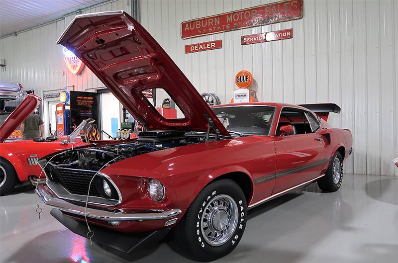 Front profile of a red Mustang with hood open in garage