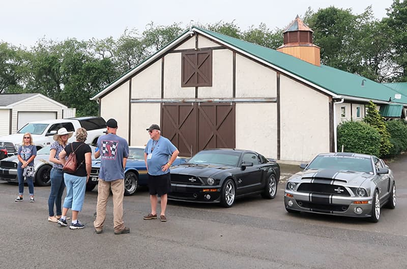 Various people and Shelbys parked outside a garage