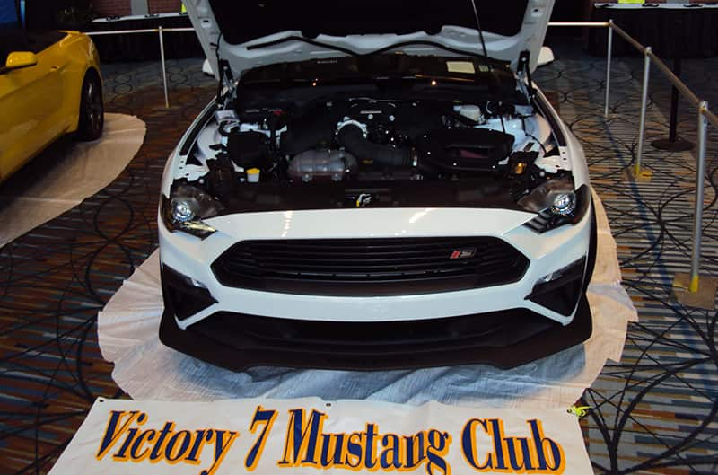 Close up front end of a white Mustang with hood open on display