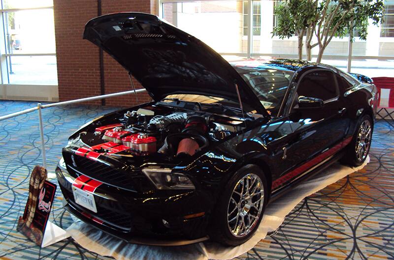 Front profile of a black Shelby GT with hood open and red stripes on display