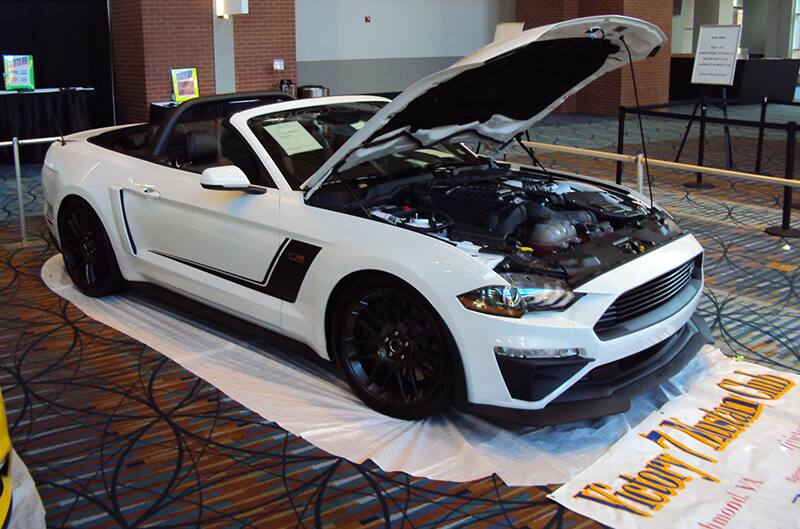 Front profile of a white Mustang convertible with hood open on display