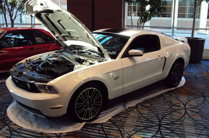 Front profile of a white Mustang GT with hood open on display