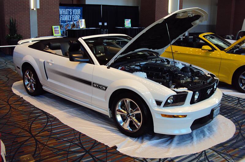 Front profile of a white Mustang GT convertible with hood open on display