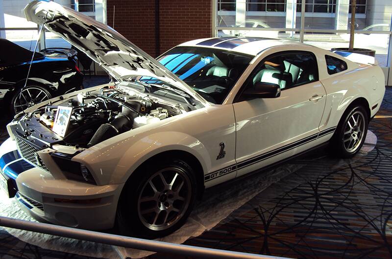 Front profile of a white Mustang GT with hood open on display