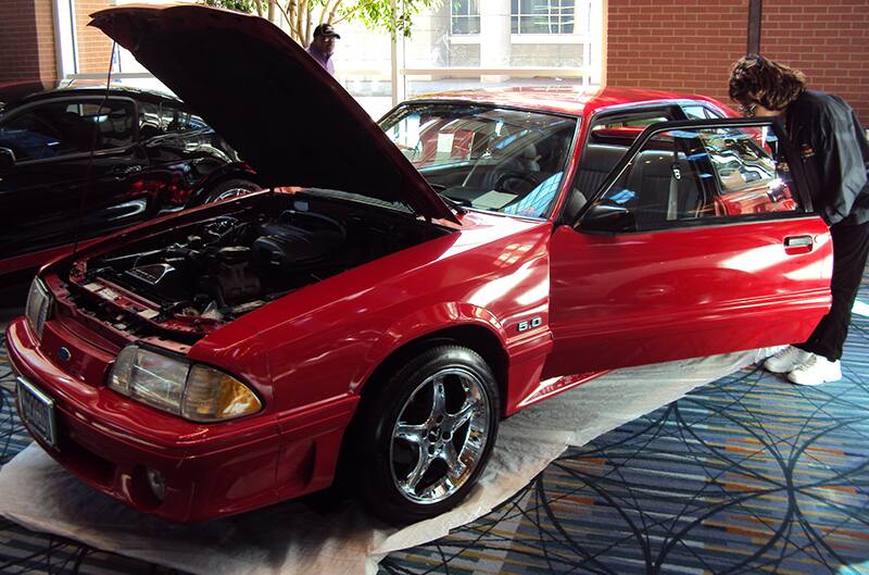 Front profile of a red Mustang with hood and door open on display