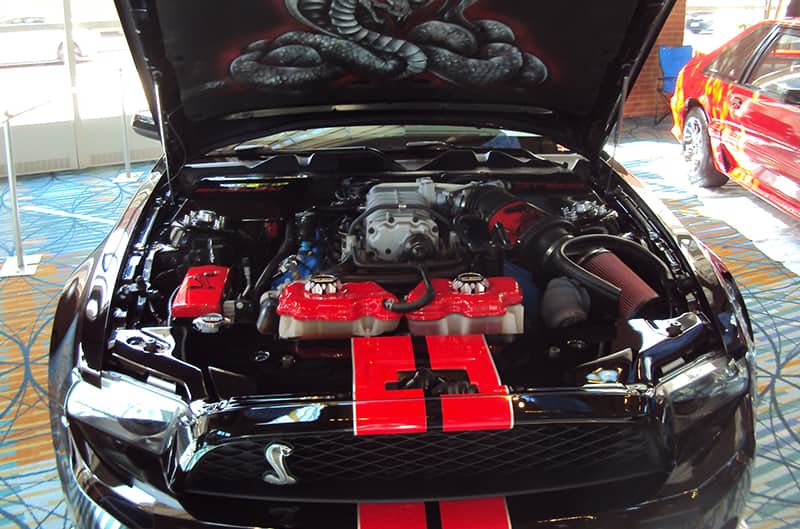 Close up front of a black Shelby Mustang with red stripes and hood open