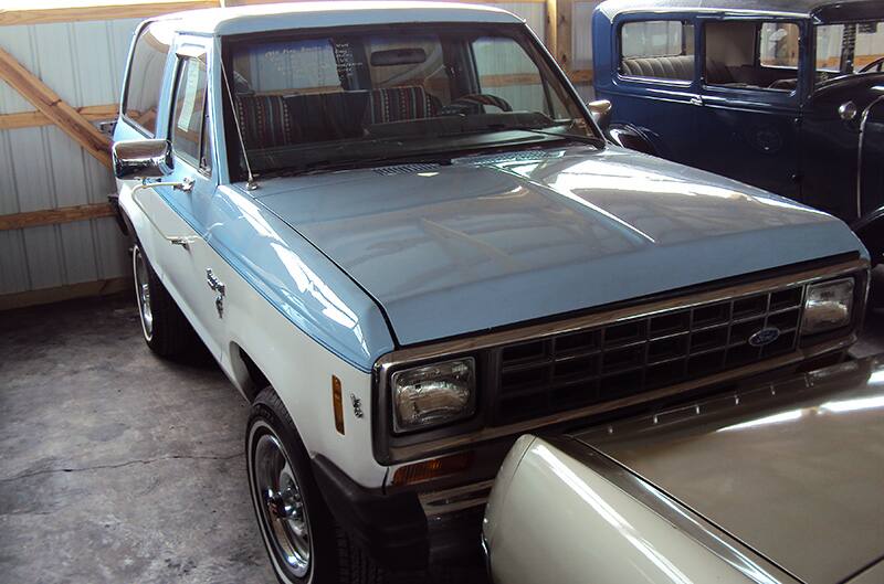 Blue and white 1980s Ford Bronco parked among other cars