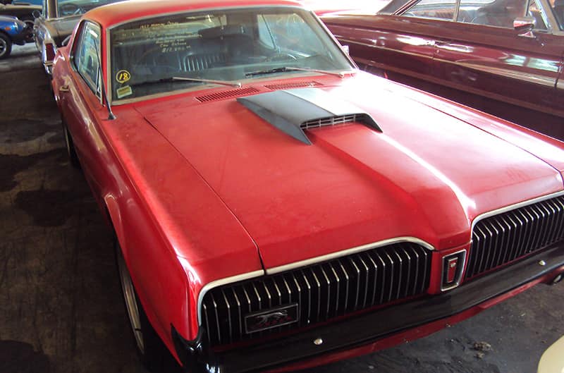 Orange Cougar covered with dust among other vehicles