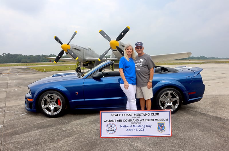 Blue S197 ROUSH Mustang with couple standing in front of XP 82 WWII plane