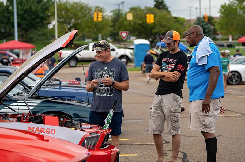 three people gathered around open hood of mustang