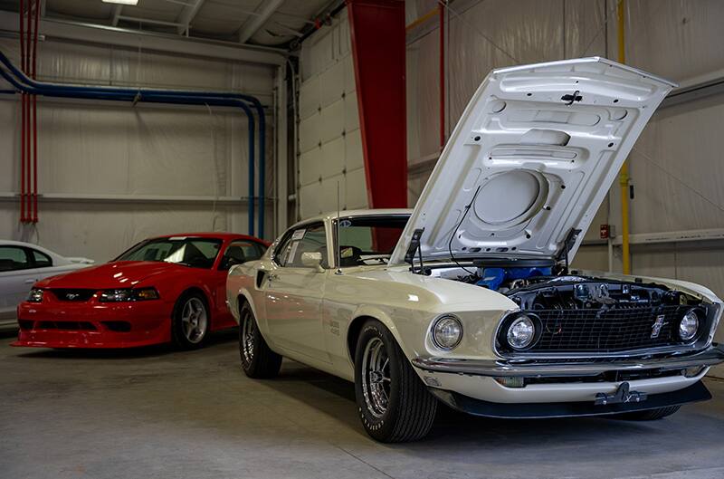 First gen mustang in white and Cobra R inside shop