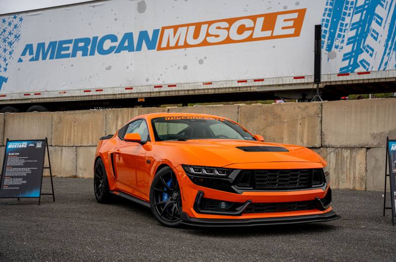 orange mustang on display in front of american muscle sign