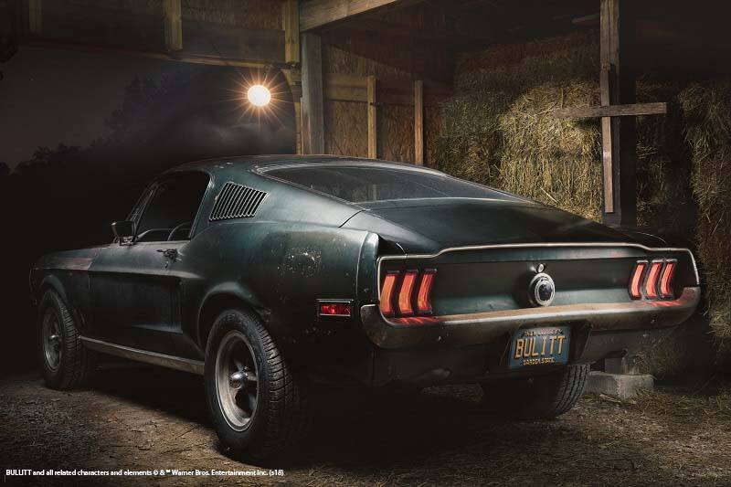 A back view of the original 1968 Bullitt Mustang parked inside a barn filled with hay