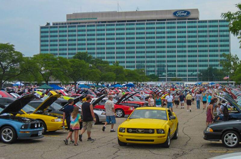 A large group of people looking at Ford vehicles on display in the parking lot of Ford World Headquarters