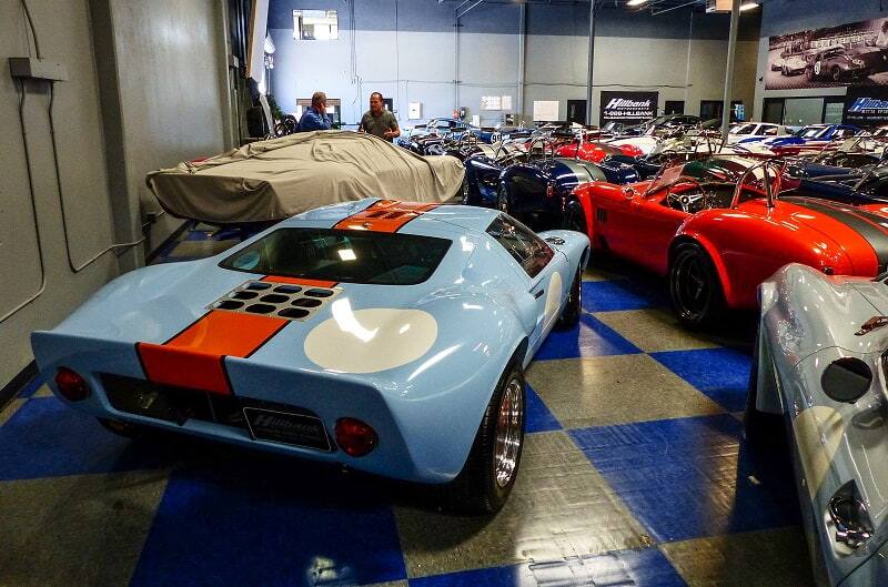 Rear of blue and orange Shelby GT in garage with various Shelbys around it