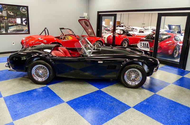 Profile of black Shelby Cobra with various red Shelbys in the background