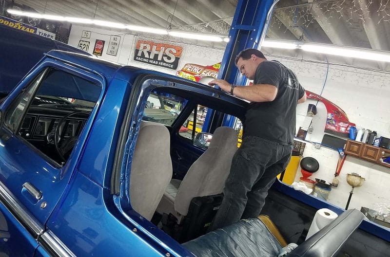 Man standing in blue Bronco looking at hood in a garage