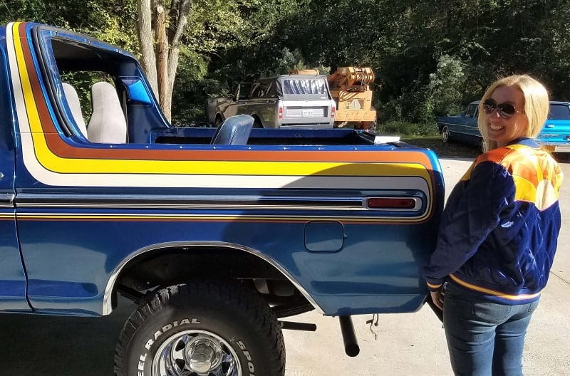 Bronco girl posing next to trunk of blue Bronco with trunk hatch off